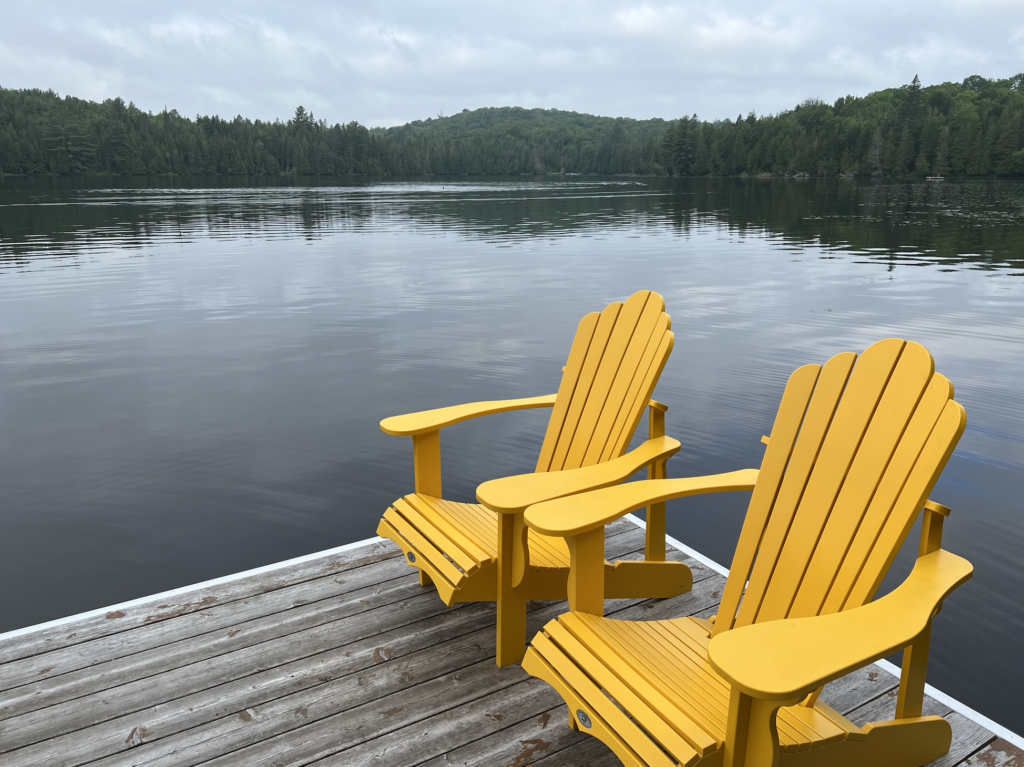 human to human podcast two yellow wooden chairs on corner on gray wood dock over lake with forest and mountain in background